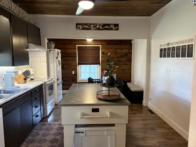 This kitchen features dark cabinetry, stainless steel appliances, a central island, and wood-paneled walls.