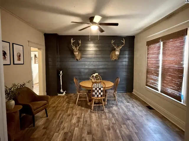 This dining area features wood-look flooring, a ceiling fan, and a dark paneled accent wall.