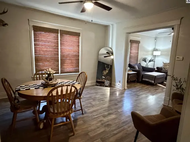 Wood-tone flooring and a ceiling fan accent this dining area with an adjacent living room.