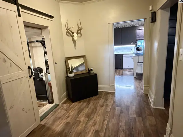This hallway features wood-look flooring, a barn door, and a dark cabinet with a mirror.