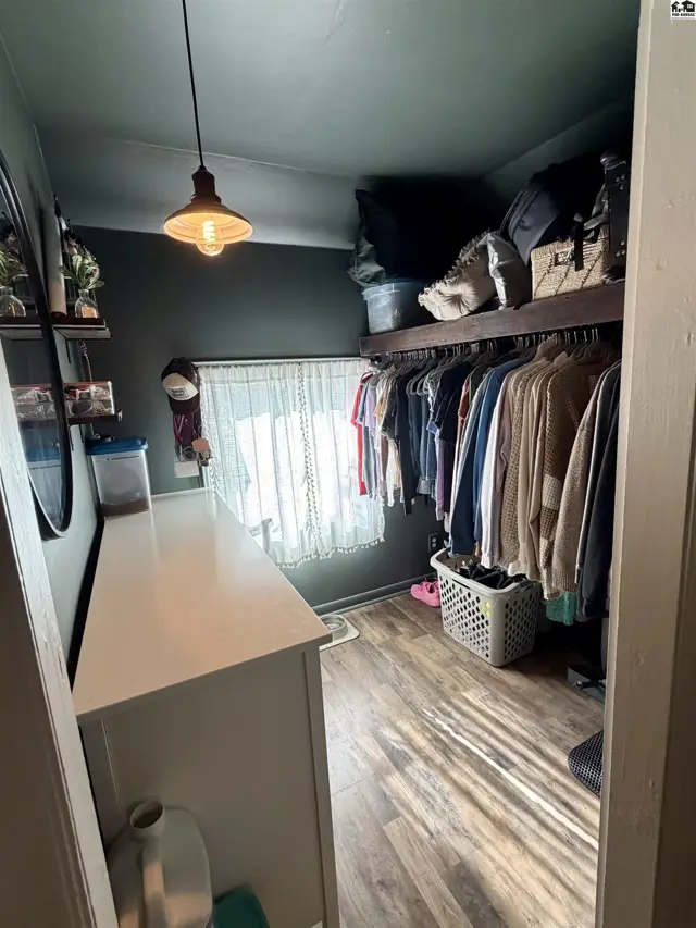 This room features a dresser, shelves, a hanging closet, and a window with a curtain.