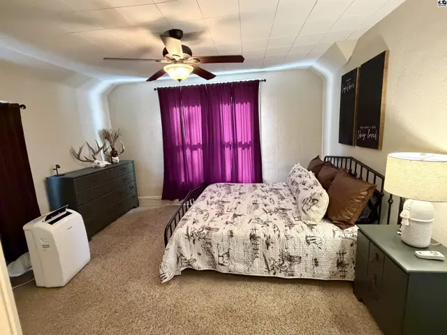 Spacious bedroom with a metal bed frame, dresser, and plush carpeting.