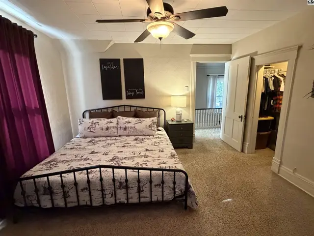 Carpeted bedroom with a ceiling fan, metal bed frame, and open closet.