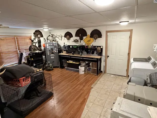 This room features wood flooring, a workbench, and a door leading to a tiled area with appliances.