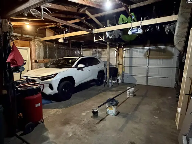 Attached garage with concrete floor, wood-framed ceiling, and a white overhead door.