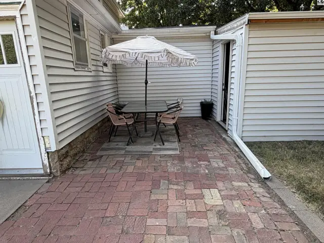 Brick patio with a table, chairs, and umbrella next to a white-sided structure.