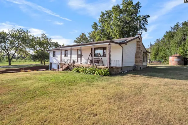 White siding home with a covered porch, stone chimney, and surrounding green lawn.