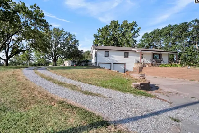 White house with a gravel driveway and mature trees on a spacious lot.