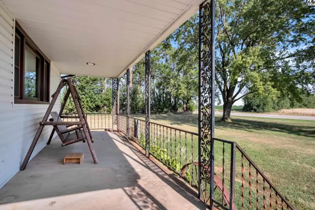 Covered porch with a swing and decorative metal railings overlooks a grassy yard.