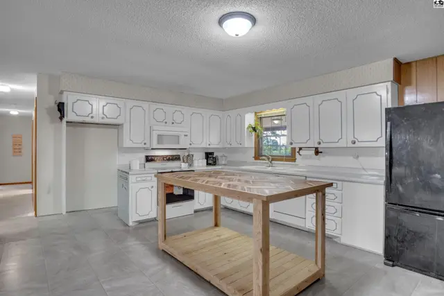 Spacious kitchen features white cabinetry, a central island, and a black refrigerator.