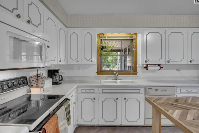 White cabinetry with decorative trim surrounds a sink and window above a countertop.