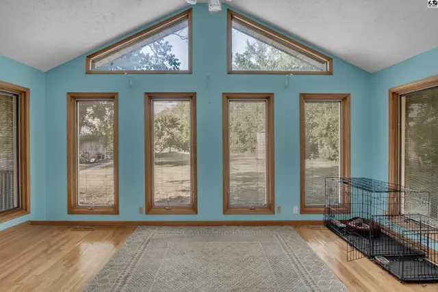 Vaulted ceiling room with light blue walls, hardwood floors, and large windows.