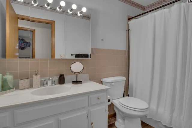 This bathroom features a white vanity, toilet, and a beige tiled shower surround.