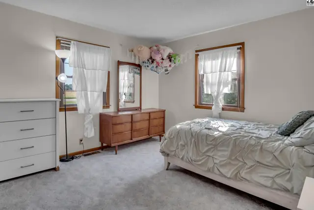 This bedroom features a bed, dresser, and two windows with white curtains.