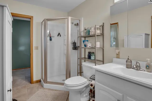 This bathroom features a corner shower, white vanity, and tiled floors.