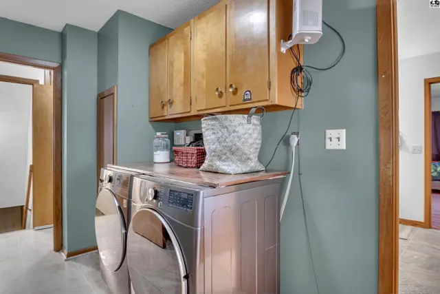 This laundry room features a stacked washer and dryer, wood cabinetry, and teal walls.