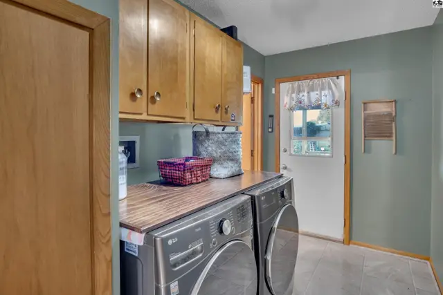 This laundry room features wood cabinetry, a built-in countertop, and a side-by-side washer and dryer.