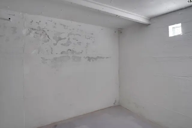 Concrete block walls with a painted finish surround this unfinished room with a small window.