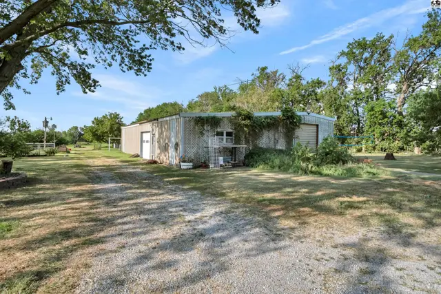 Metal-sided building with two garage doors and surrounding mature trees.