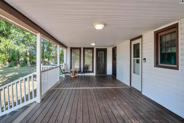 Spacious covered porch with wooden deck, white railing, and ceiling lights.