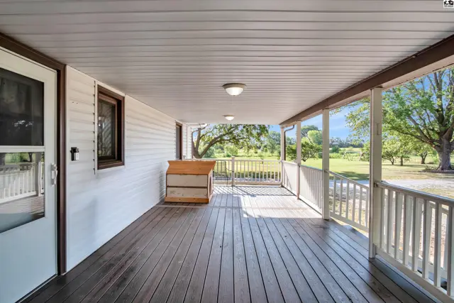 Covered porch with wood decking and white railings overlooks a grassy yard.