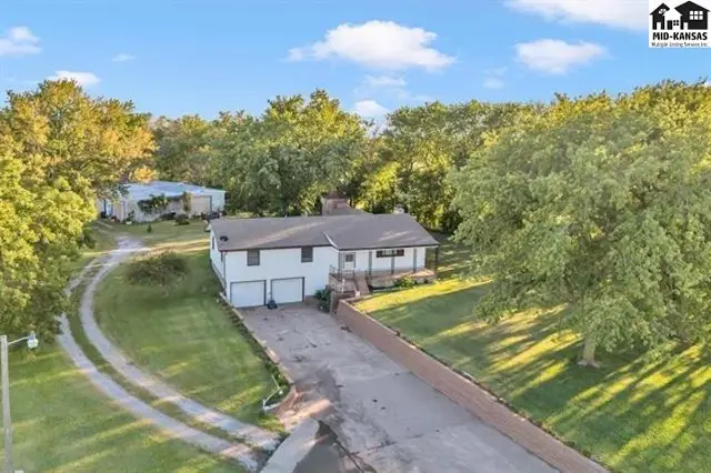 This home features a white exterior, attached two-car garage, and mature trees.