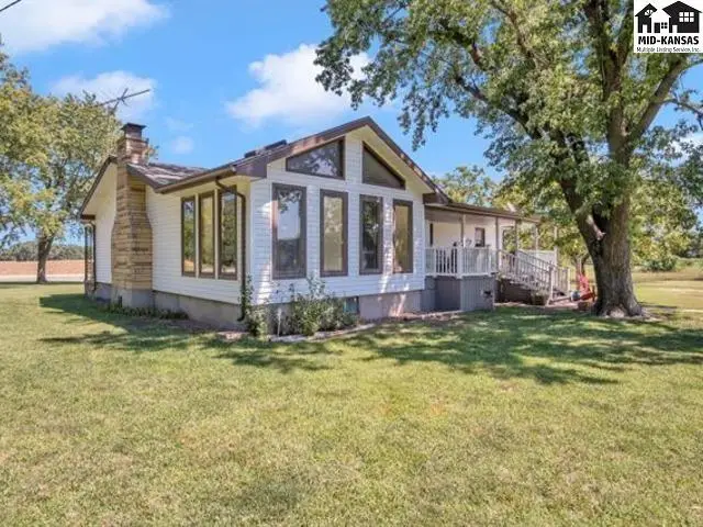 White-sided house with a stone chimney and large windows sits on a grassy lawn.