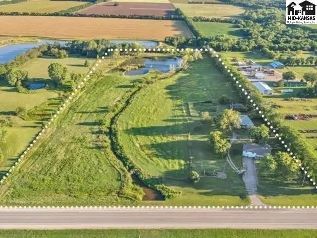 Expansive acreage features a home, outbuildings, and a pond surrounded by mature trees.
