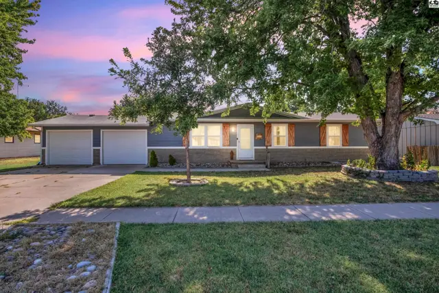 This single-story home features a gray exterior, two-car garage, and mature trees.