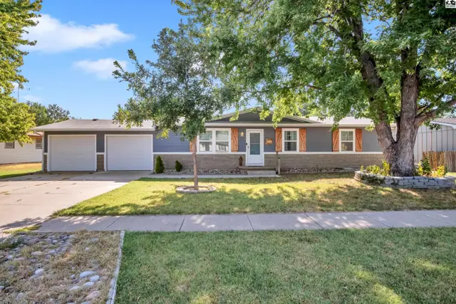 This single-story home features a gray exterior, a two-car garage, and mature trees.