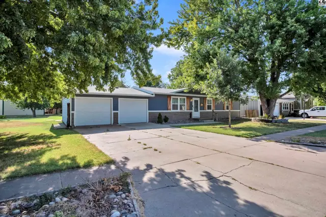 This single-story home features a dark blue exterior, a two-car garage, and mature trees.