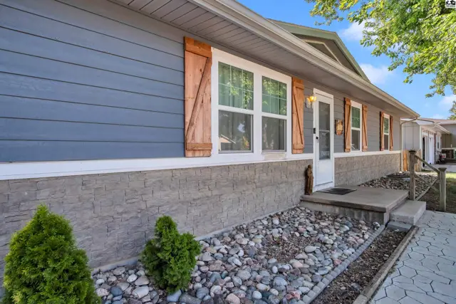Blue siding and stone exterior with wood shutters and a concrete walkway.