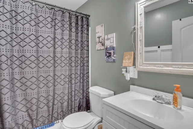 This bathroom features a white vanity, toilet, and a patterned shower curtain.