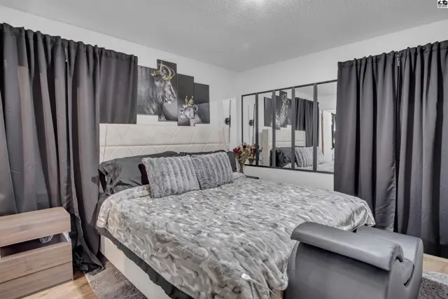 Spacious bedroom features a king-sized bed, large mirrored wall, and dark curtains.