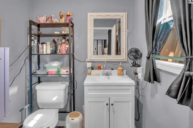 This bathroom features a white vanity, toilet, and a tall metal shelving unit.