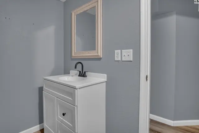White vanity with a white countertop and black faucet is below a framed mirror.