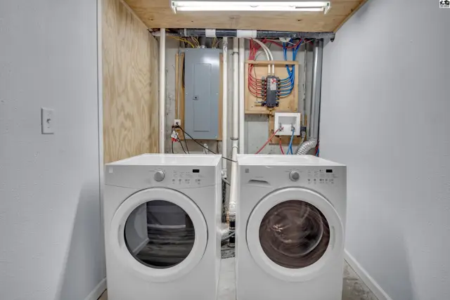This laundry room features two white appliances, a utility sink, and a visible electrical panel.