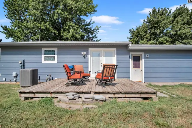 A wooden deck with seating overlooks a grassy yard with mature trees.