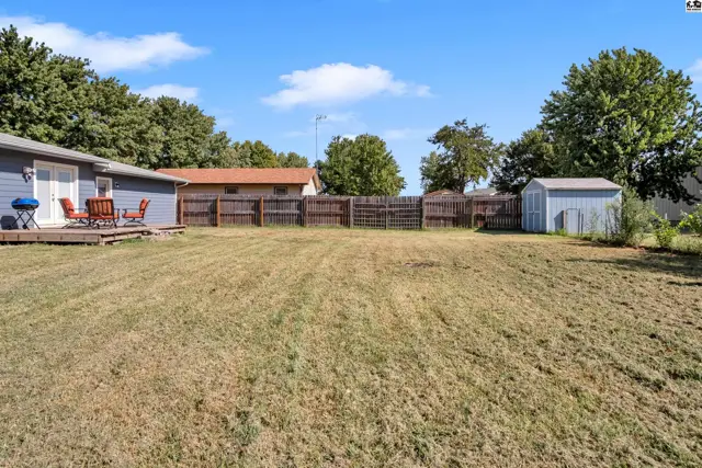 Spacious, fenced backyard with a wooden deck, shed, and mature trees.