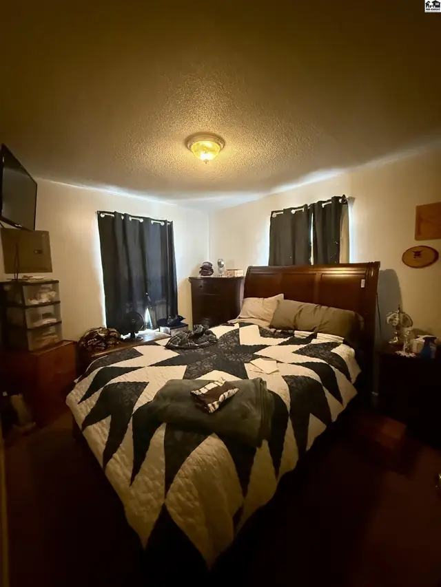 This bedroom features a queen-size bed, dark curtains, and a ceiling light fixture.