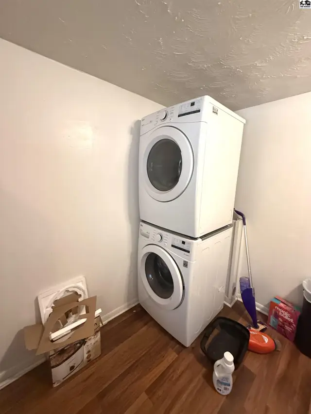 Stacked white washer and dryer units with a mop and cleaning supplies.