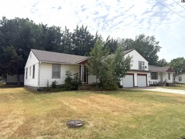 White siding house with a two-car garage and mature trees on a grassy lot.