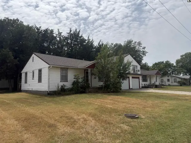 White siding ranch home with a detached garage and mature trees.
