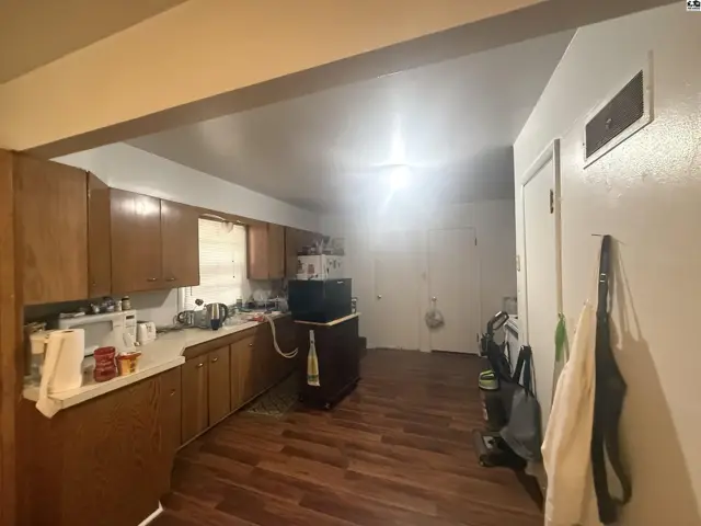 This kitchen features wood cabinetry, laminate countertops, and wood-look flooring.