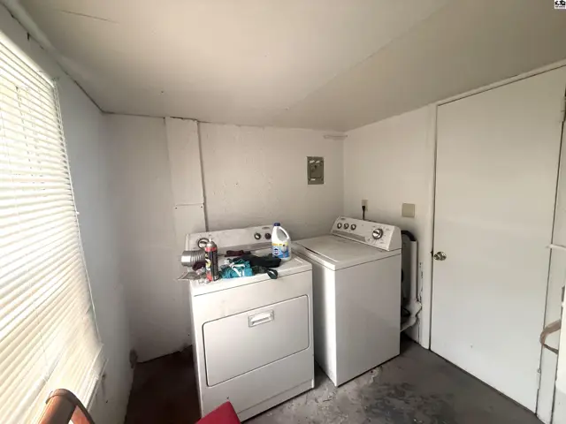 White washer and dryer set in a room with concrete floor and white walls.