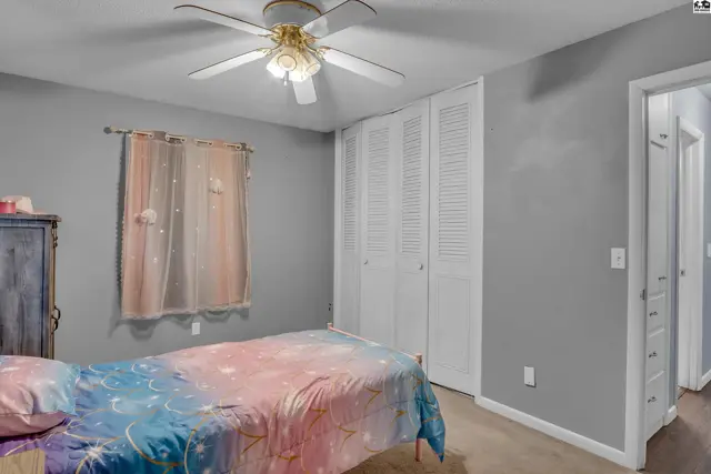 This bedroom features a ceiling fan, bi-fold closet doors, and a window with sheer curtains.