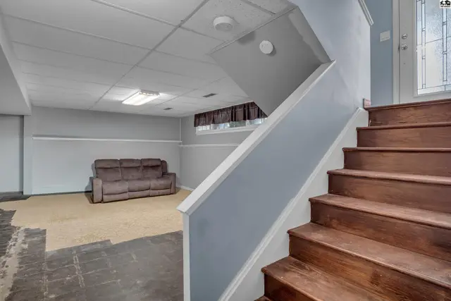 Finished basement with carpeted floor, sofa, and wood-paneled staircase.