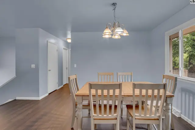 A dining room with a wooden table, six chairs, and a chandelier.