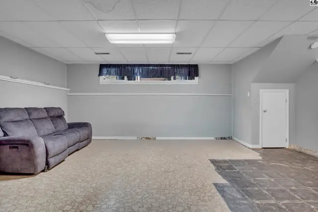 Spacious finished basement with carpeted floor, recessed lighting, and a door to unfinished space.