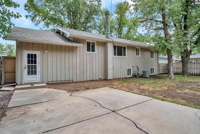This beige-sided home features a concrete patio and mature trees in the backyard.